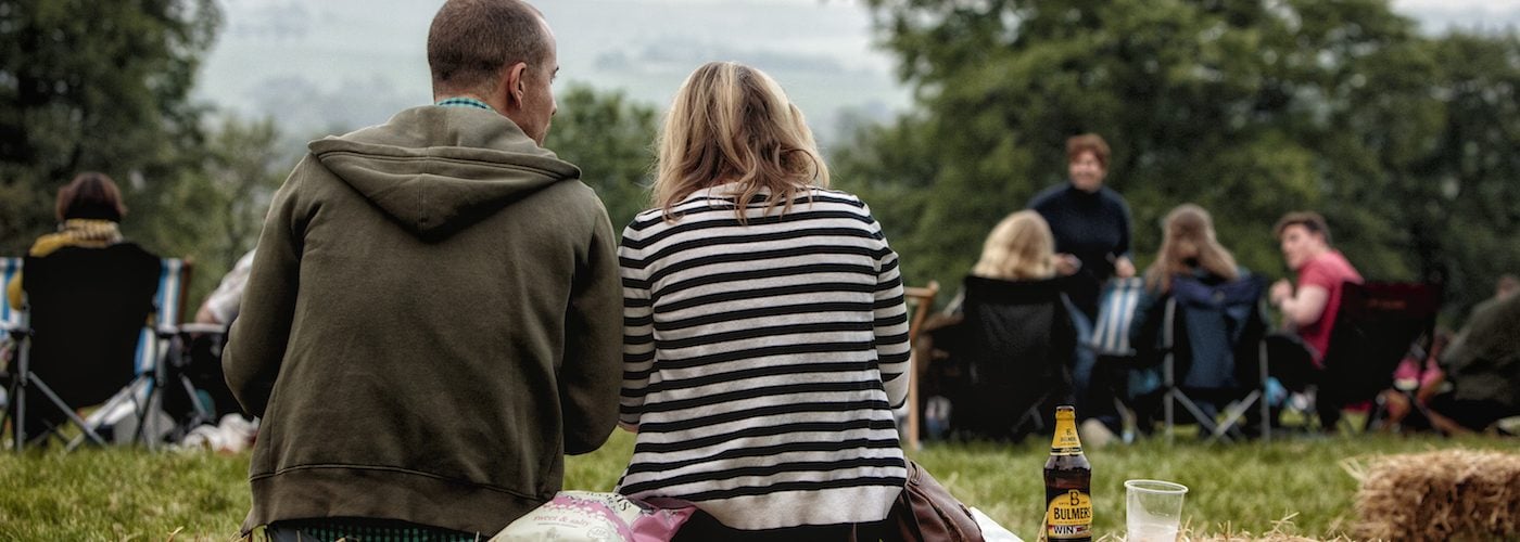 A couple cuddle up on a hay bale with a bottle of cider next to them.