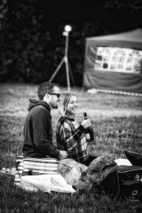 Black and white photograph of a young couple smiling and holding up a bottle of wine.