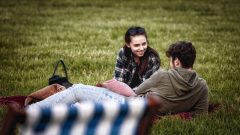 A young couple lay down on the grass deep in conversation.