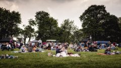 A photo of many groups of spectators gathered on a field ready to watch an outdoor movie.