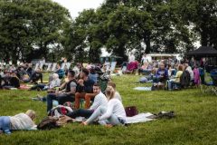 A photo of many groups of spectators gathered on a field ready to watch an outdoor movie.