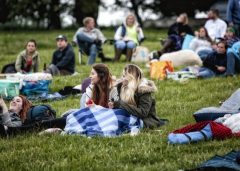 Two women are snuggled up underneath a blanket, ready for their outdoor cinema experience.