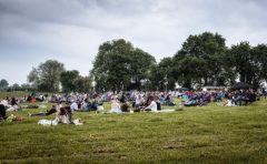 An early evening photo of a group of eventgoers relaxing on a field on camping chairs and blankets.