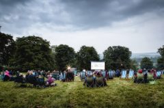 A photo of a large group of people sat in deckchairs ready for a film to start on the big screen in front of them.