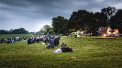 An early evening photo of a group of eventgoers relaxing on a field on camping chairs and blankets.