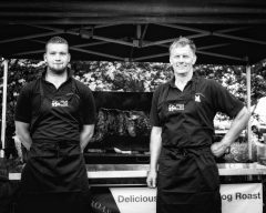Two men stand infront of a Hog Roast smiling and posing for a photo opportunity.