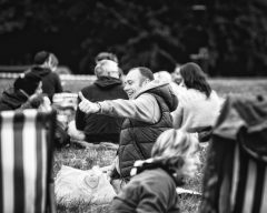 A man sits on grass at an event giving the thumbs up to someone out of shot.